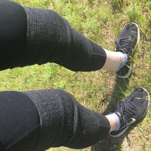 May include: A pair of black leggings with a textured pattern. The leggings are worn by a person standing on a grassy surface. The person is wearing black sneakers with white accents.