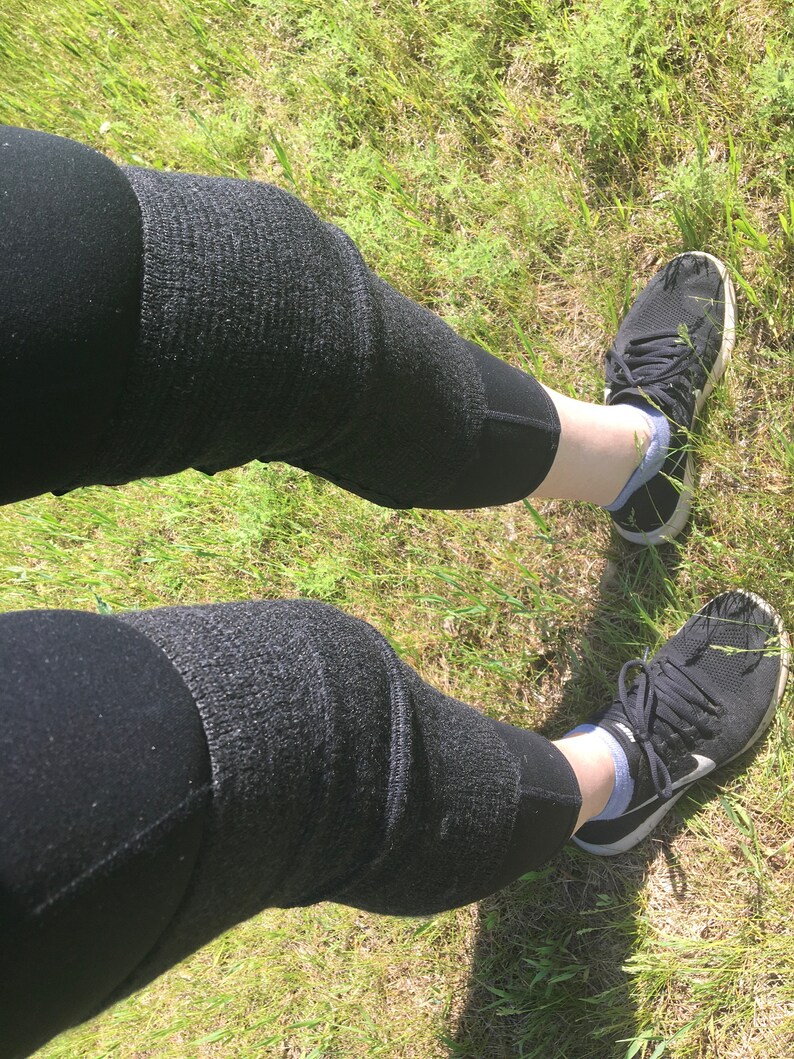 May include: A pair of black leggings with a textured pattern. The leggings are worn by a person standing on a grassy surface. The person is wearing black sneakers with white accents.
