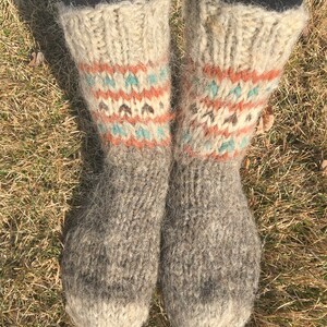 May include: A pair of grey wool socks with a white cuff and colourful geometric patterns. The socks are fuzzy and have a rustic look.