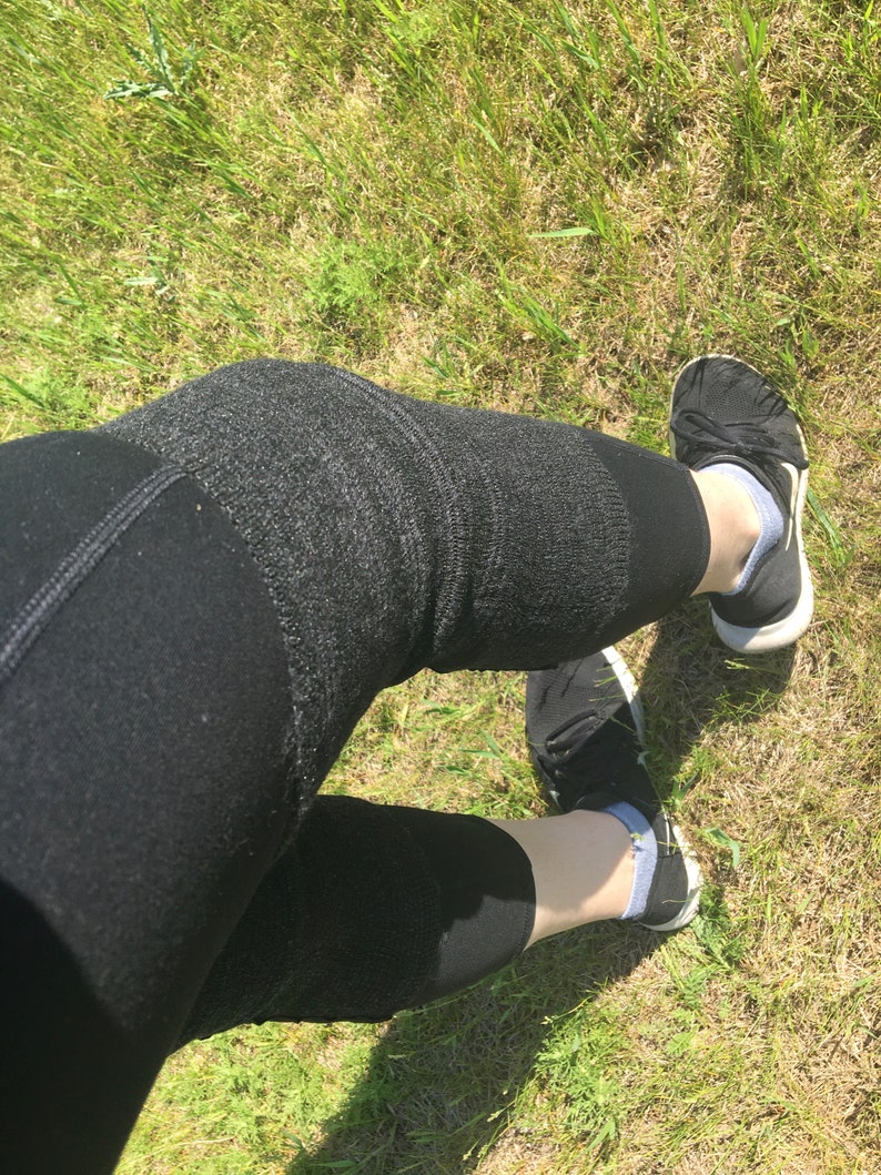 May include: A pair of black leggings with a textured pattern. The leggings are worn by a person standing on a grassy surface. The person is wearing black shoes with white soles.