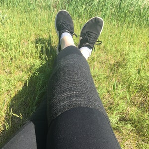May include: A person wearing black leggings and black sneakers with white soles, sitting in a grassy field.