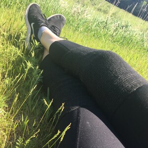 May include: A person wearing black leggings and black sneakers is lying on their back in a grassy field.