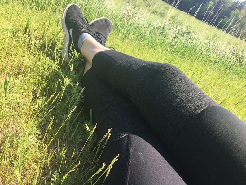 May include: A person wearing black leggings and black sneakers is lying on their back in a grassy field.