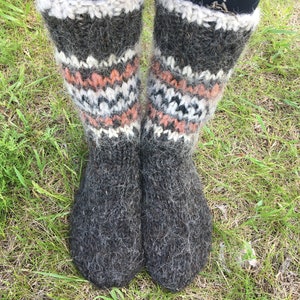 May include: A pair of gray wool socks with white and orange stripes. The socks are knitted and have a fuzzy texture.