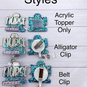 May include: Three different styles of nurse badge reels with a blue and turquoise glitter background. The text "Nurse in Progress" is on each reel. The first reel is an acrylic topper only. The second reel has an alligator clip. The third reel has a belt clip.