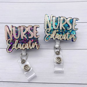 May include: Two glitter nurse educator badge reels with white text and gold trim. The badge reels are on a white wood background.