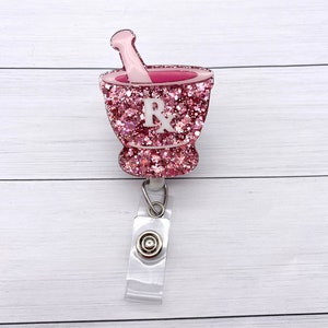 May include: Pink glitter mortar and pestle with a white "Rx" on the side, attached to a clear retractable badge reel.