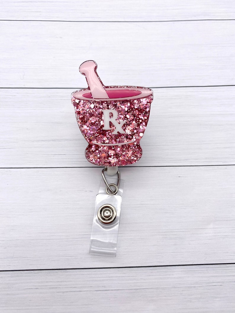 May include: Pink glitter mortar and pestle with a white "Rx" on the side, attached to a clear retractable badge reel.