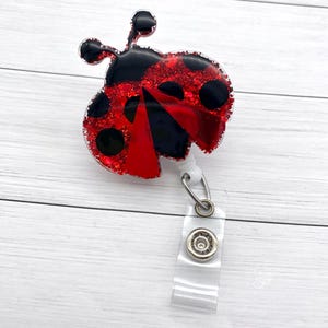May include: Red and black glitter ladybug with black dots, attached to a clear plastic retractable badge holder.