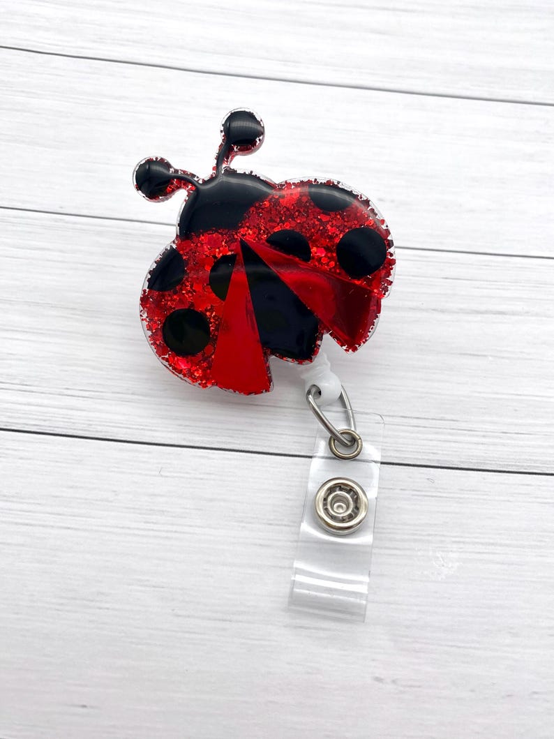 May include: Red and black glitter ladybug with black dots, attached to a clear plastic retractable badge holder.