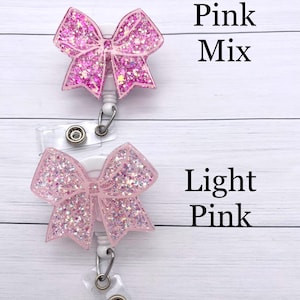 K&ouml;nnte beinhalten: Zwei rosa glitzernde Schleifen-Ausweishalter. Der obere ist mit "Pink Mix" und der untere mit "Light Pink" beschriftet.