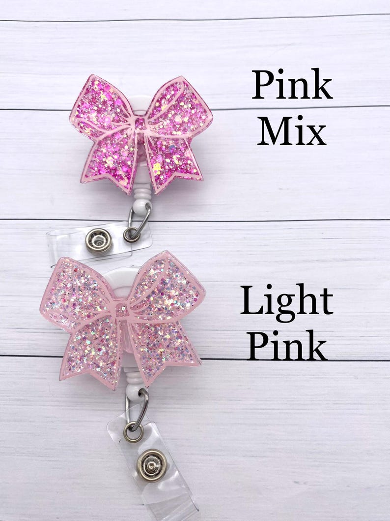 K&ouml;nnte beinhalten: Zwei rosa glitzernde Schleifen-Ausweishalter. Der obere ist mit "Pink Mix" und der untere mit "Light Pink" beschriftet.