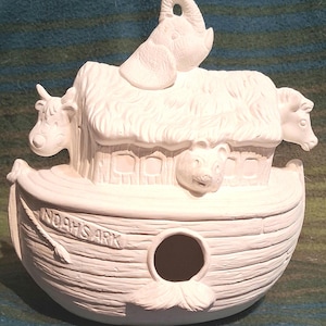 May include: A white ceramic Noah's Ark figurine with an elephant, two cows, and a bear on top. The ark has a round opening and the words "NOAH'S ARK" are carved on the side. The figurine is unpainted and ready for customization.