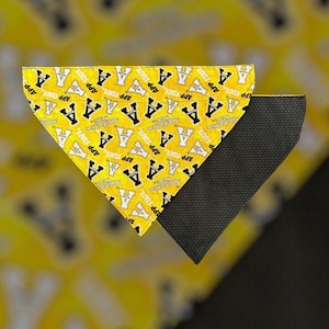 May include: A triangular pet bandana featuring a yellow fabric with a repeating black and white Appalachian State logo and text pattern. The reverse side of the bandana is made of a solid black fabric with a fine, textured, grid-like surface pattern.