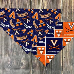 May include: Two triangular pet bandanas featuring University of Virginia branding. One bandana has a dark blue background with repeating orange V logos, crossed sabers, and the text Virginia and Wahoos. The other has a grid of orange and blue squares.