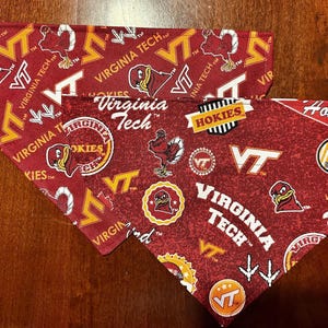 May include: Two triangular fabric pet bandanas featuring a maroon background with repeating Virginia Tech logos, the Hokies mascot, and the text Virginia Tech and Hokies in white and orange. The fabric pattern includes various university-themed graphics.