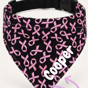 A black bandana with a pink ribbon pattern, featuring the name "Cooper" written in white on the right side.