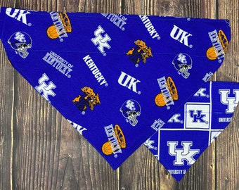 Może przedstawiać: Dwie niebiesko-białe bandany dla psa z motywem Kentucky Wildcats. Większa bandana ma powtarzający się wzór logo UK, piłek do koszykówki i napis "University of Kentucky". Mniejsza bandana ma powtarzający się wzór logo UK w białym kwadracie na niebieskim tle.
