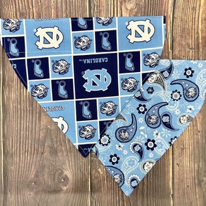 May include: Two dog bandanas, one with a blue and white paisley pattern and the other with a blue and white pattern featuring the University of North Carolina Tar Heels logo and the words "Carolina TM".