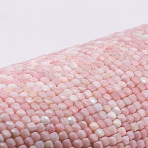 May include: Close-up of a roll of pink gemstone beads. The beads are small, faceted, and have a range of pink hues. The beads are arranged in a tightly packed pattern, creating a textured surface.