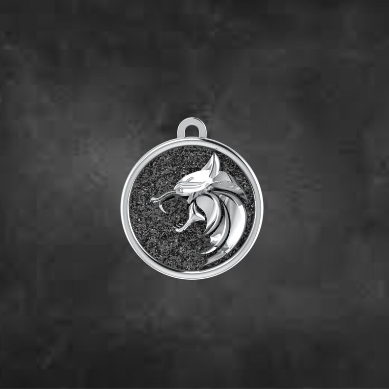 May include: A silver pendant featuring a lion's head in profile, with an open mouth, set against a textured, dark grey background within a circular frame. The pendant has a loop for a chain.