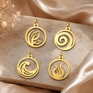 Könnte beinhalten: Vier goldfarbene Anhänger mit verschiedenen Designs: ein Blatt, eine Spirale, eine Welle und eine Flamme. Jeder Anhänger ist kreisförmig mit einer kleinen Schlaufe für eine Kette. Sie werden auf einer strukturierten, hellbraunen Oberfläche präsentiert.