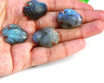 Puede incluir: Cuatro figuras de peces de labradorita tallada en tonos azules, grises y verdes se muestran en una mano. Los peces tienen escamas y aletas detalladas, con un acabado pulido. Las figuras son pequeñas, decorativas y adecuadas para coleccionistas.