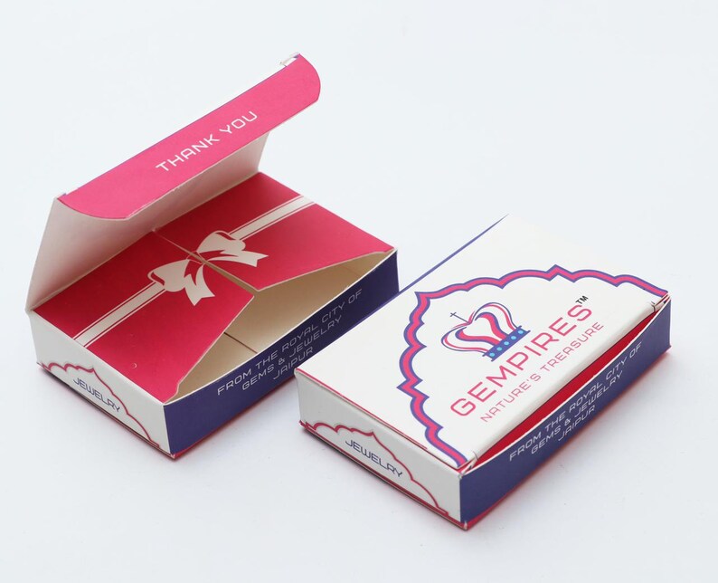 May include: Two jewellery boxes, one open and one closed, on a white surface. The open box is red with a white bow design and the words "THANK YOU". The closed box is white with the text "GEMPIRES NATURE'S TREASURE".