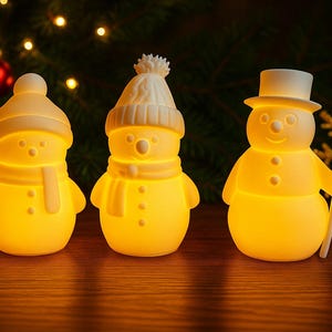 Könnte beinhalten: Drei leuchtende Schneemannfiguren mit Hüten und Schals. Einer hält einen Besen. Die Schneemänner leuchten und erzeugen eine warme, festliche Atmosphäre. Weihnachtsdekoration.
