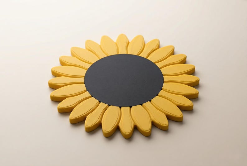 May include: A decorative sunflower-shaped object with a black center and yellow petals. The petals are rounded and arranged in a circular pattern. The object is likely made of a solid material and rests on a neutral surface.