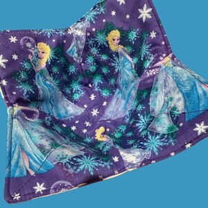 May include: Purple fabric bowl with a white trim and a snowflake pattern. The bowl features images of a character from the movie Frozen wearing a blue dress.