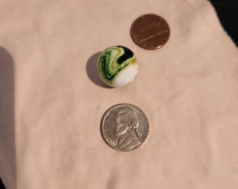 May include: A white glass marble with green and black swirls. The marble is about the size of a US penny.