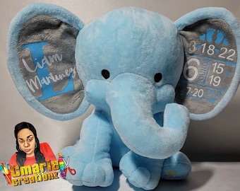 May include: A light blue plush elephant with gray ears. The ears are personalized with the name "Liam Martinez" and the date "3-18-22" with the time "7:20" and weight "6 lbs 15 oz".