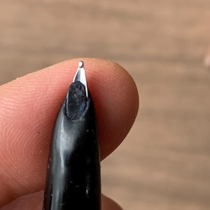 Pu&ograve; includere: Primo piano di un pennino di penna stilografica nero. Il pennino &egrave; argentato e presenta una piccola fessura. Il corpo della penna &egrave; nero e lucido. Lo sfondo &egrave; sfocato e di tono neutro.