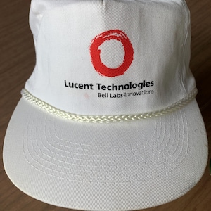 May include: White baseball cap with a curved brim and a braided rope detail. The cap features the text "Lucent Technologies" and "Bell Labs Innovations" below a red circular logo.