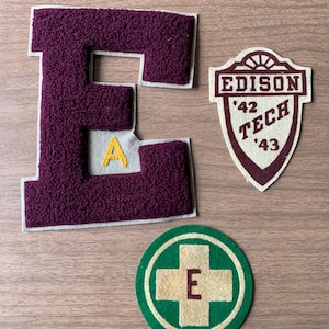 May include: Three vintage school patches. A large maroon letter "E" with a white border and a small yellow "A" inside. A shield-shaped patch reads "Edison Tech '42 '43". A green and cream circular patch has a cross and the letter "E".