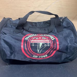 May include: Black duffel bag with a red and white logo that says "The Rolling Stones North America LA 2015 Zip Code".
