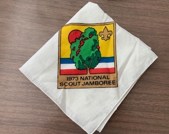 Pode incluir: Bandana de algodão branco com um remendo marrom, amarelo, vermelho, azul e verde. O remendo apresenta uma árvore, um sol, um símbolo scout e o texto "1973 National Scout Jamboree".