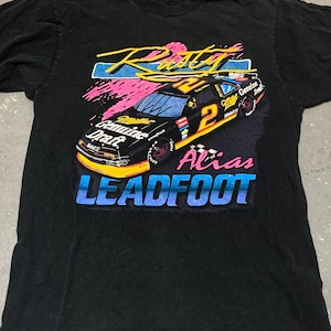 May include: Black t-shirt featuring a race car design with the text "Rusty Alias LEADFOOT". The graphic includes the number 2, sponsor logos, and a colorful design with pink, blue, and yellow accents. The shirt is vintage.
