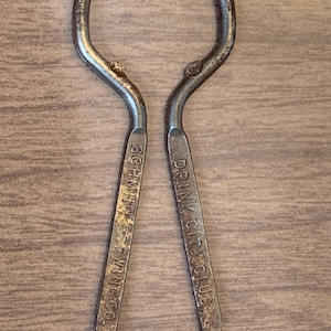 May include: A vintage metal bottle opener with the words "Drink City Club" and "Schlitz Brewing Co." printed on it.