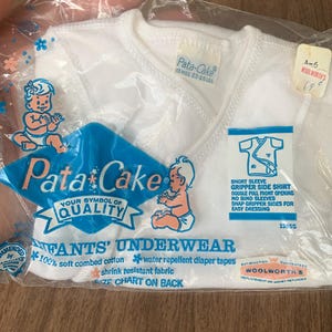 May include: A package of white infant underwear, labeled "Pata-Cake," with a blue and white logo featuring a baby illustration. The package includes details about the product's features, such as soft combed cotton and water-repellent diaper tapes.