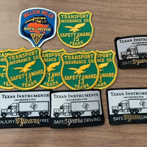 May include: A collection of eight embroidered patches featuring various safety awards and logos. The patches are green, yellow, and black with white lettering. The patches feature logos for "Million Miler", "Transport Insurance Co.", and "Texas Instruments Incorporated".