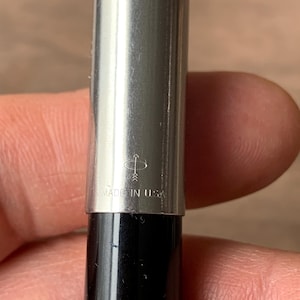 Pu&ograve; includere: Primo piano di una penna d'argento con base nera. La penna ha una finitura metallica lucida e il testo "MADE IN USA" &egrave; visibile. &Egrave; visibile anche il logo della penna.