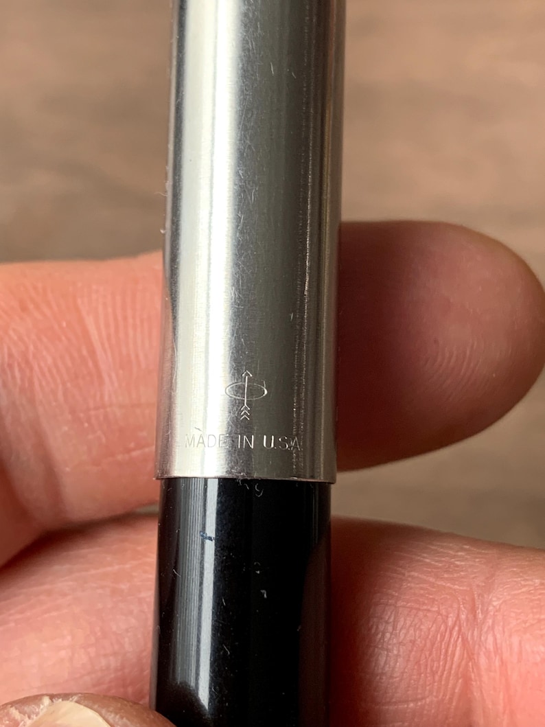 Pu&ograve; includere: Primo piano di una penna d'argento con base nera. La penna ha una finitura metallica lucida e il testo "MADE IN USA" &egrave; visibile. &Egrave; visibile anche il logo della penna.