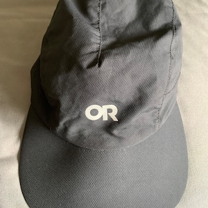 May include: A black,  Outdoor Research (OR) branded,  running cap with a curved brim.