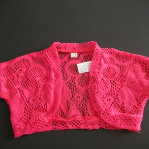 May include: A pink crocheted shrug with short sleeves and a floral pattern.