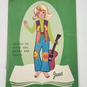 以下が含まれることがあります： DOLL cutout BOOKというタイトルの緑色の紙人形切り抜きブック。表紙には「clothes for every day, parties and sports」という文字が書かれています。緑のシャツ、紫のベスト、太陽のデザインが施された青いベルボトムパンツを着用し、ギターを持った金髪のキャラクターのイラストが描かれています。