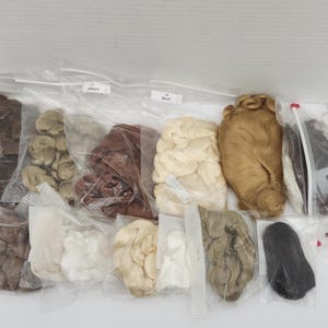 May include: A collection of synthetic doll wigs in various colors including black, brown, blonde, white, and grey, each individually packaged in clear plastic zip-top bags. The assortment features different hair textures and lengths for dolls.