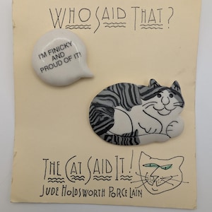 May include: A vintage porcelain cat figurine with a speech bubble that reads "I'm finicky and proud of it!" The cat is gray and white, lying down on a cream-colored card with the text "Who Said That?" and "The Cat Said It!"