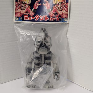 May include: A vintage Japanese action figure of a skeletal humanoid, encased in a clear plastic bag. The figure is primarily white and gray with black accents. The packaging features illustrations of menacing creatures and Japanese text.